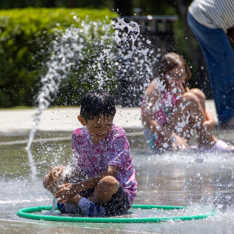 young boy sitting in water spout of splash pad playing with the water