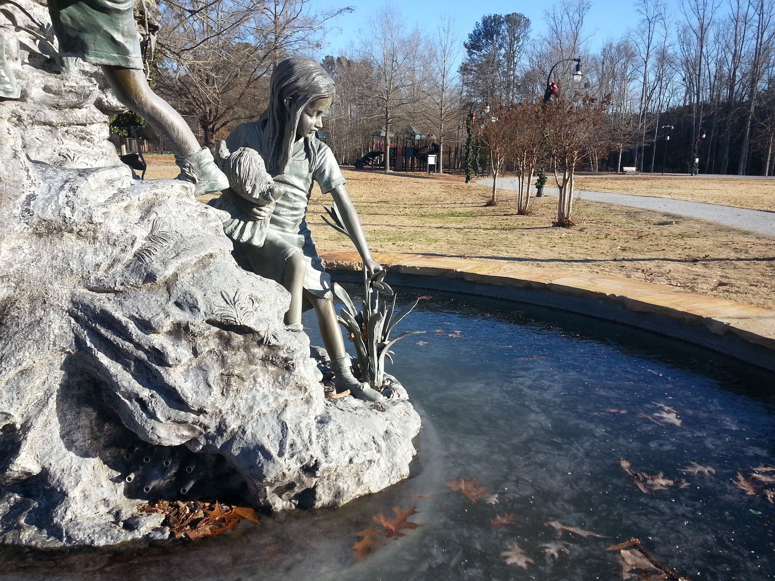 sculpture in the center of a fountain of kids climbing a rock and touching plants
