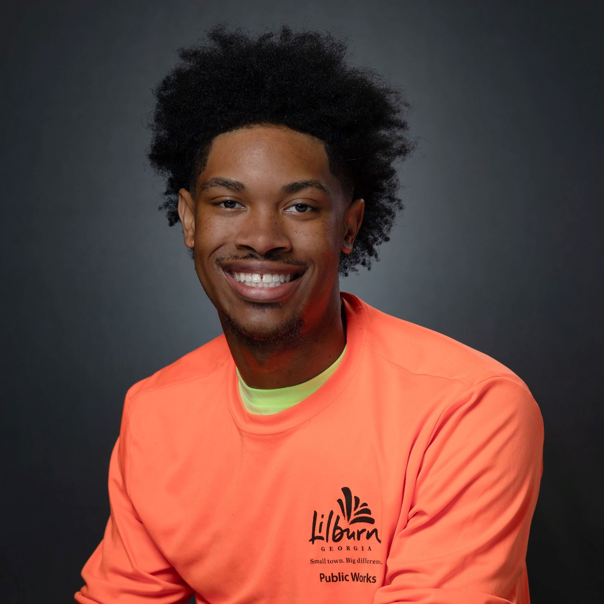 Headshot of Travis Card male with small afro wearing orange long sleeve tee