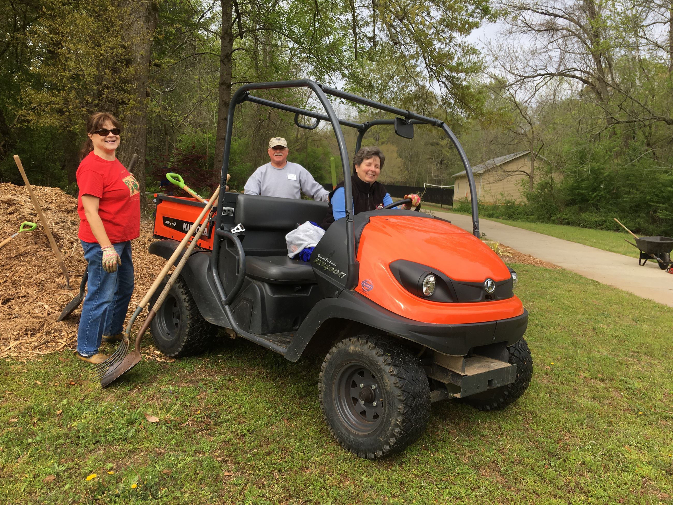 a male and two female gardeners pose with shovels, mulch and a Kubota UTV